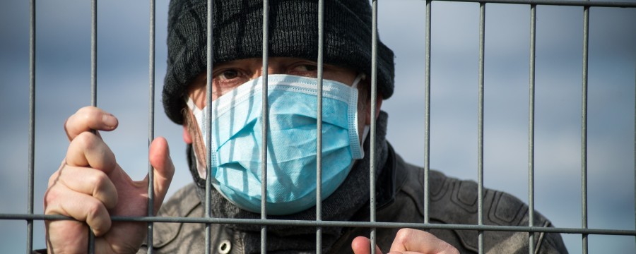 Ein Mann mit Maske hinter einem Zaun.