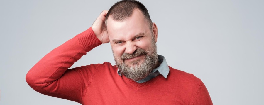 Mann mit rotem Pullover kratzt sich verwirrt am Kopf.
