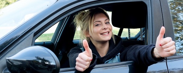 junge Frau sitzt im Auto und streckt den Daumen hoch