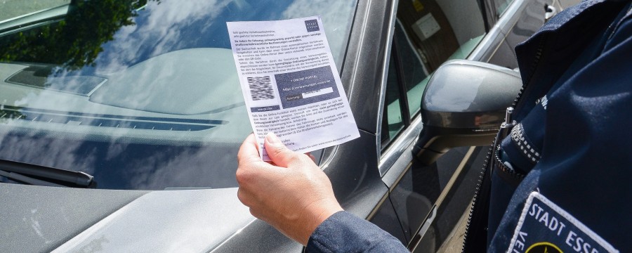 Ordnungsamtsmitarbeiterin verteilt ein Knöllchen mit QR-Code