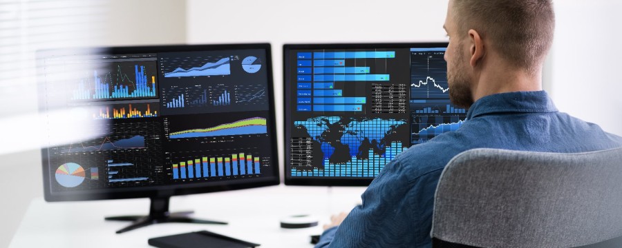 Mann analysiert Daten auf  zwei Bildschirmen
