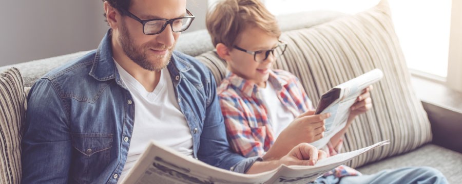 Vater und Sohn lesen Zeitung auf der Couch.