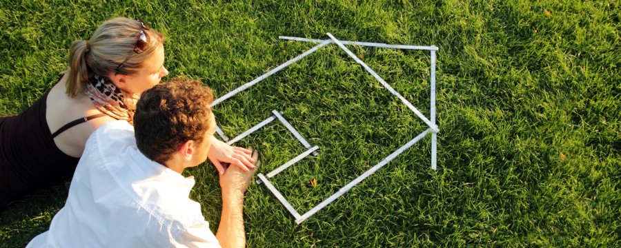 Frau und Mann im Gras mit Haus aus Zollstock
