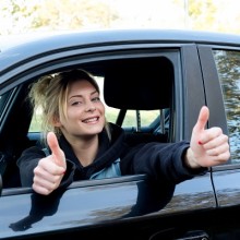 junge Frau sitzt im Auto und streckt den Daumen hoch