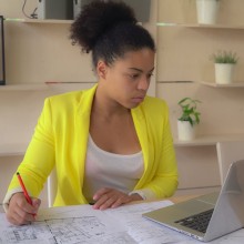 Frau sitzt mit Bauplan vor Notebook 