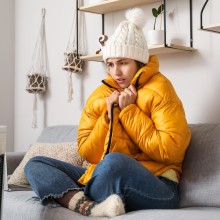 Frau sitzt frierend auf der Couch