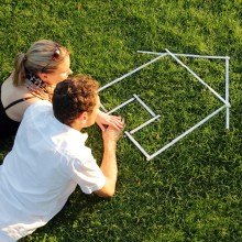 Frau und Mann im Gras mit Haus aus Zollstock