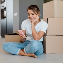 Frau mit Smartphone vor Umzugskartons
